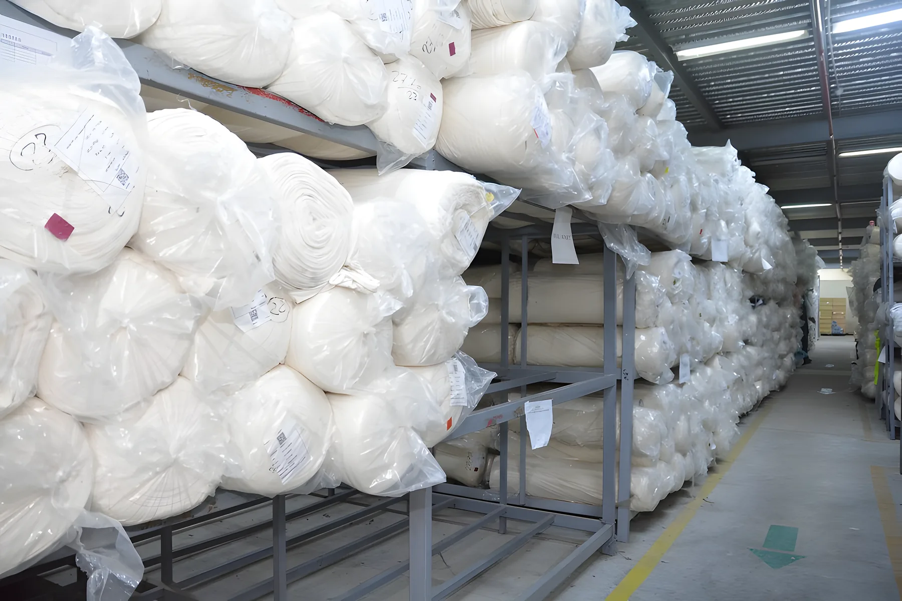 Wrapped rolls of white knit fabric on steel racks in the fabric store