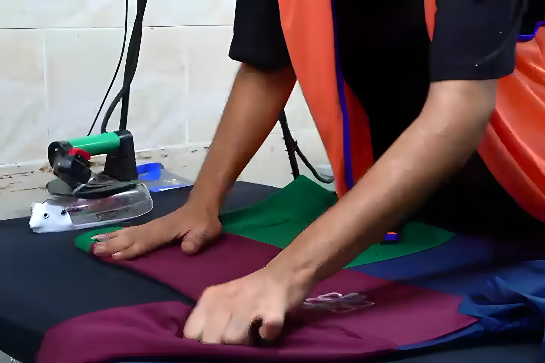 An operator presses a garment with a steam iron at the finishing table